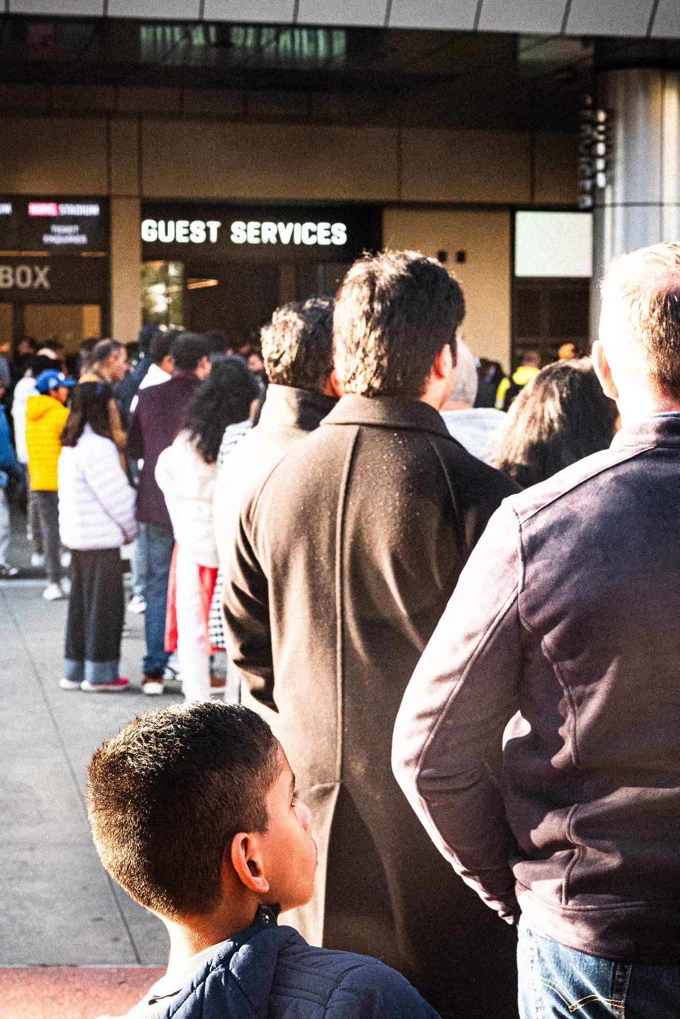 Backs of heads stacked up the frame in the queue beneath the Guest Services sign