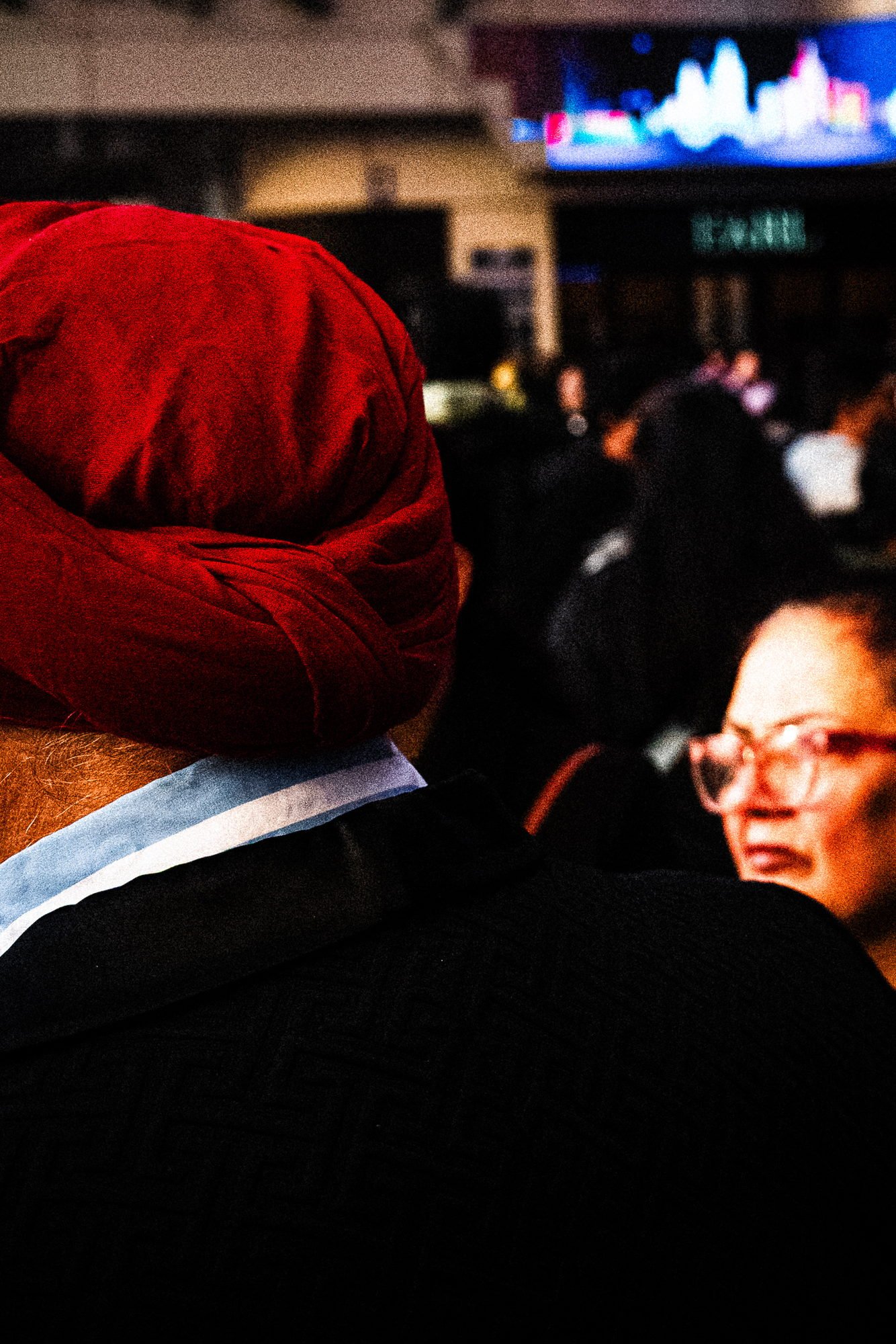 Back of a red turban with a woman in glasses watching past it