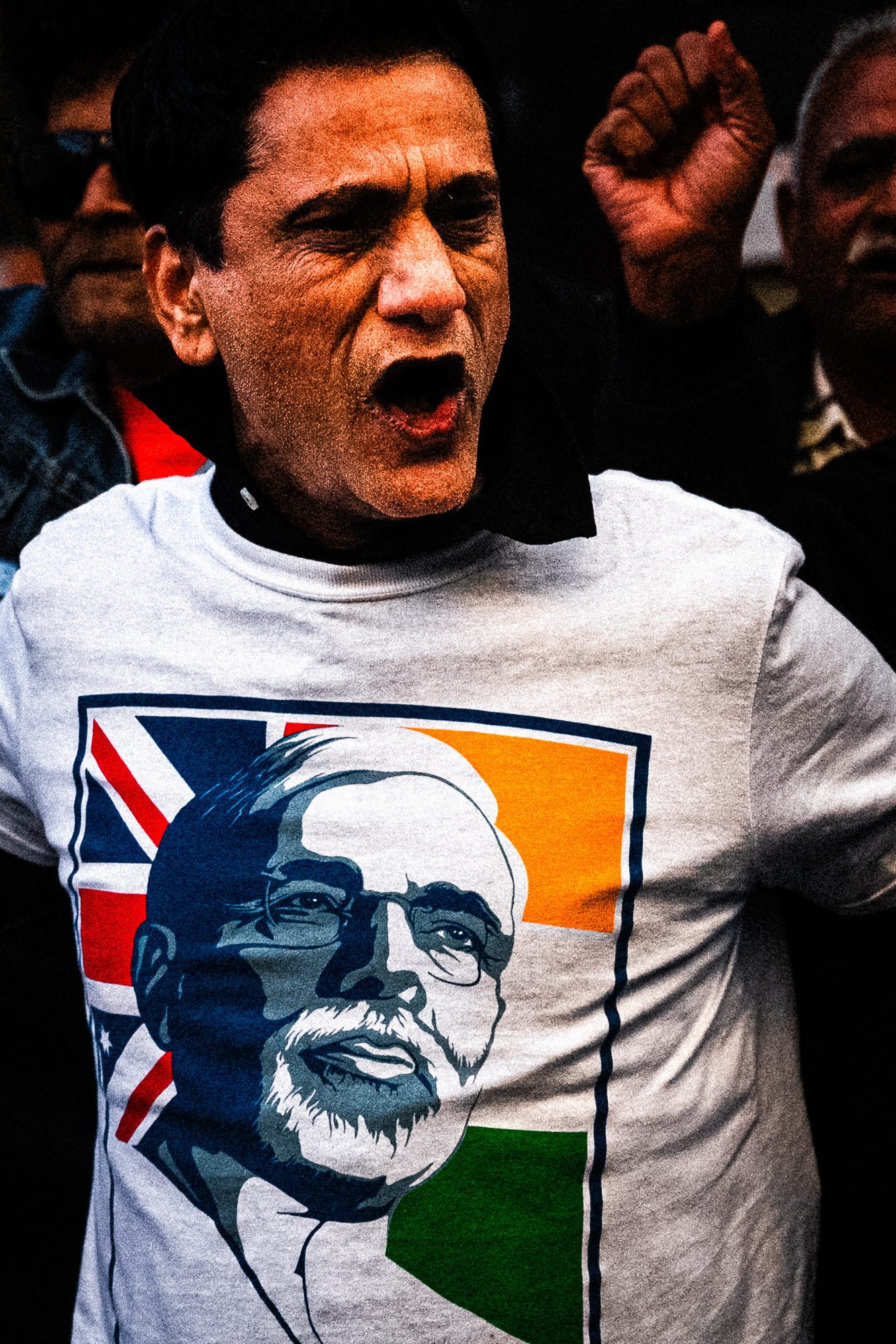 Man mid shout in a white t-shirt printed with Modi's portrait over both flags, a raised fist behind him