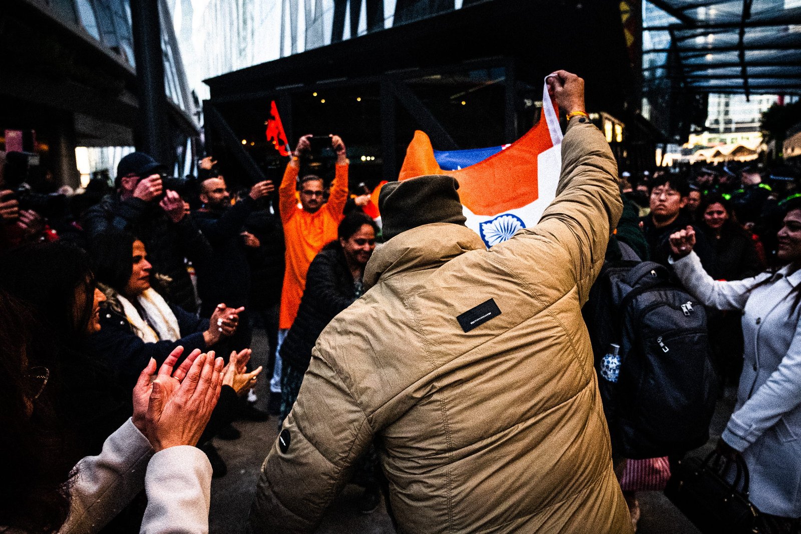 Fist raised above a tan puffer jacket, tricolour over the shoulder, hands clapping at the left edge