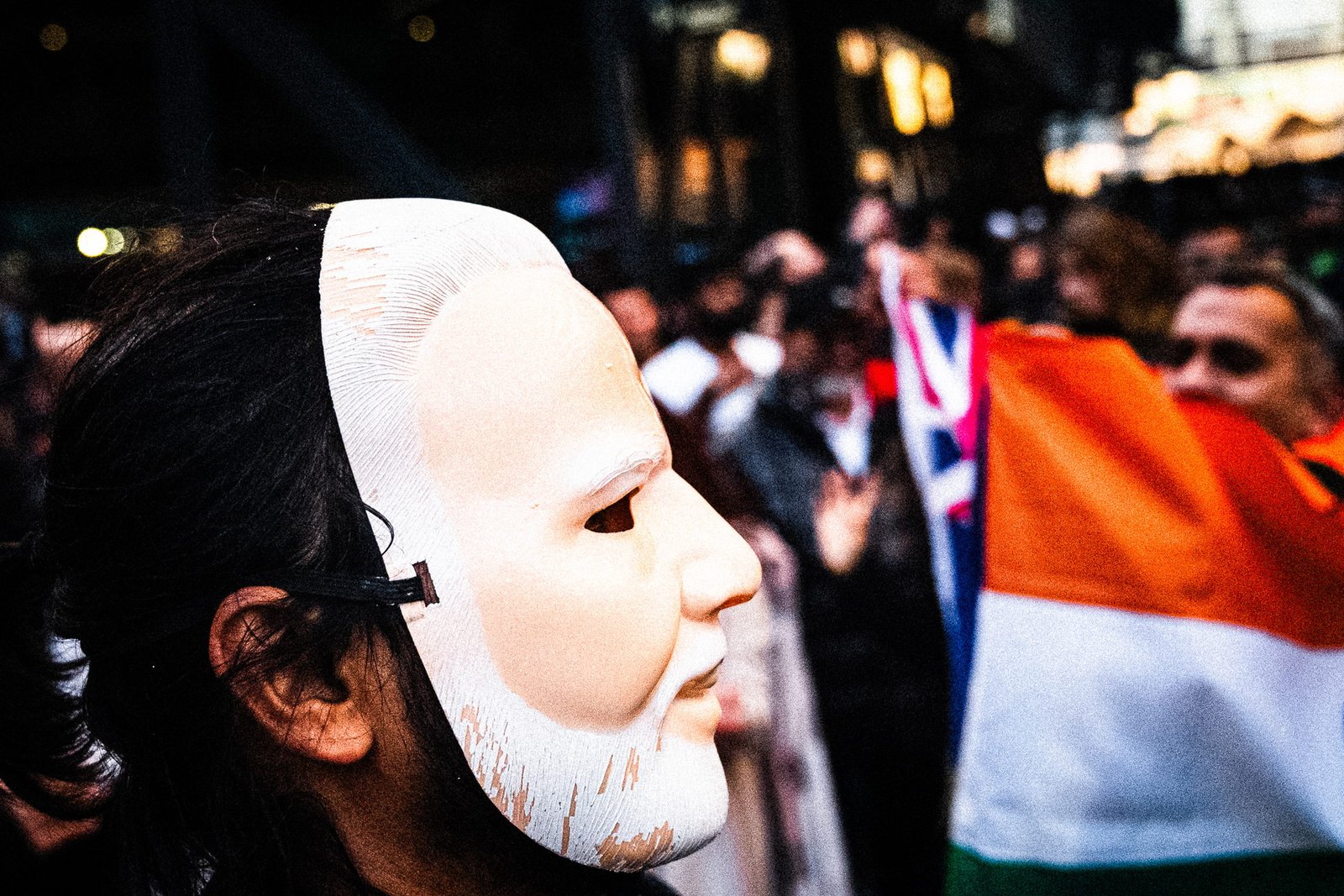 A Modi mask worn on the side of a woman's head, her own ear and hair beside its profile